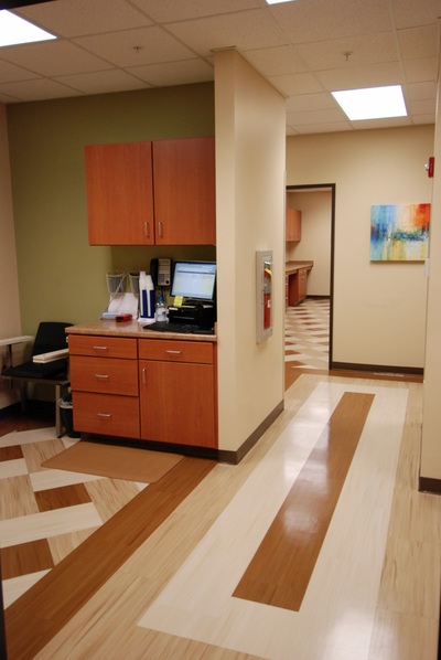 side view of vitals and blood draw station with neutral geometric flooring leading into hallway with colorful, abstract watercolor painting