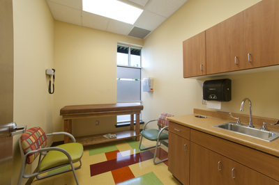 Pediatric Partners of Augusta exam room with light tone wooden cabinets and exam table with colorful geometric patterned chairs and flooring 