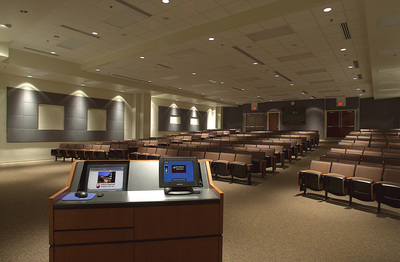 auditorium inside of Canter Medical Services Building with rows of folding chairs and a large podium at the front with computers