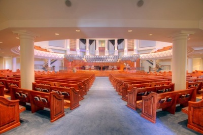 back view of wooden pews leading up to open circular pulpit with light blue carpeting at First Baptist Church of North Augusta 