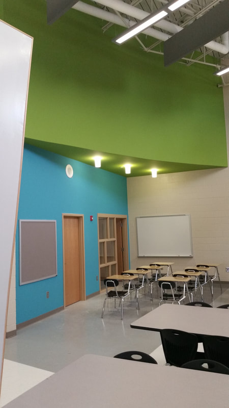bright blue accent wall and lime ceiling with light wooden accents, white board and student desks