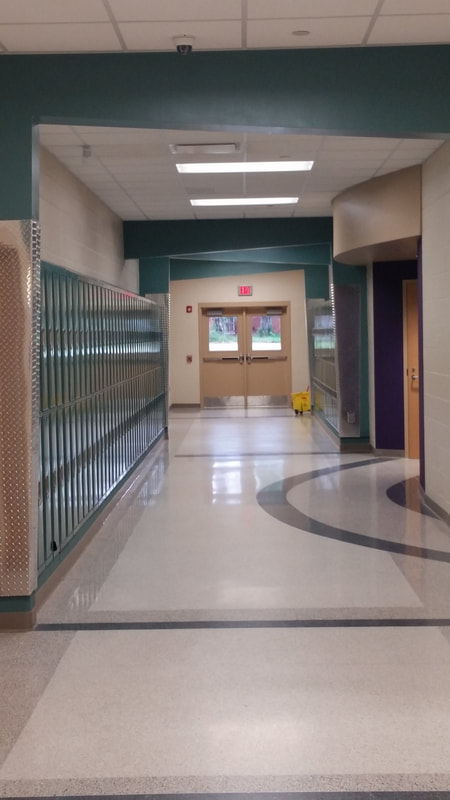 exit doors at the end of hallway with teal lockers and purple and off white graphic flooring