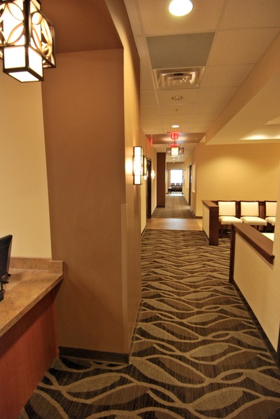 partial view of waiting area down hallway with neutral patterned carpeting and warm lighting