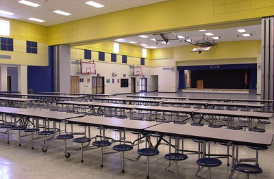 Craig houghton elementary school cafeteria with long tables with attached chairs and bright yellow accents on the upper half of the walls