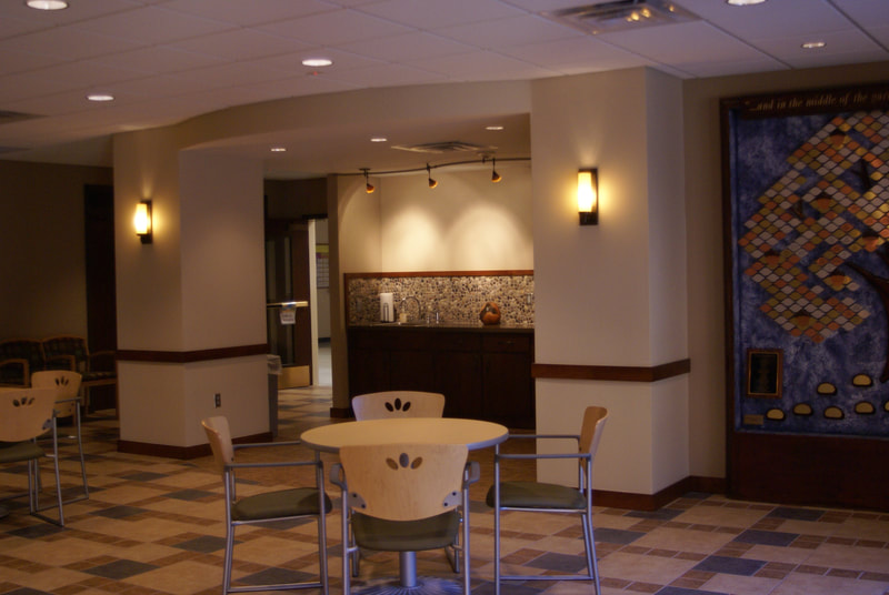 view towards restroom area featuring lighted sconces, a table and chairs and partial view of large tree artwork 