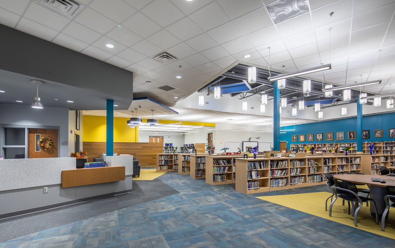 Butler High School library with yellow accent wall, sky blue accent wall, low shelving filled with books and grey front desk and librarian's station 