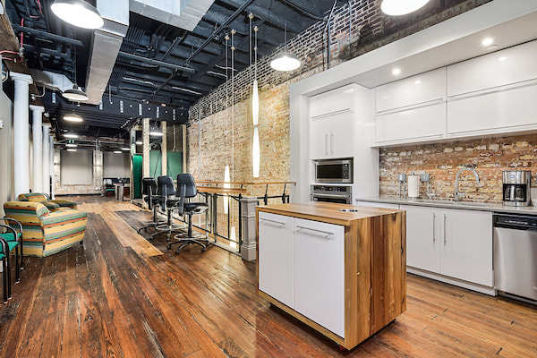 break room and kitchenette area for destination Augusta employees, with bright white cabinetry, open bar height tables, and decorative green accents