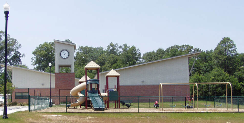 side view of McBean Community Center in brick and vinyl with playground jungle gym and swings