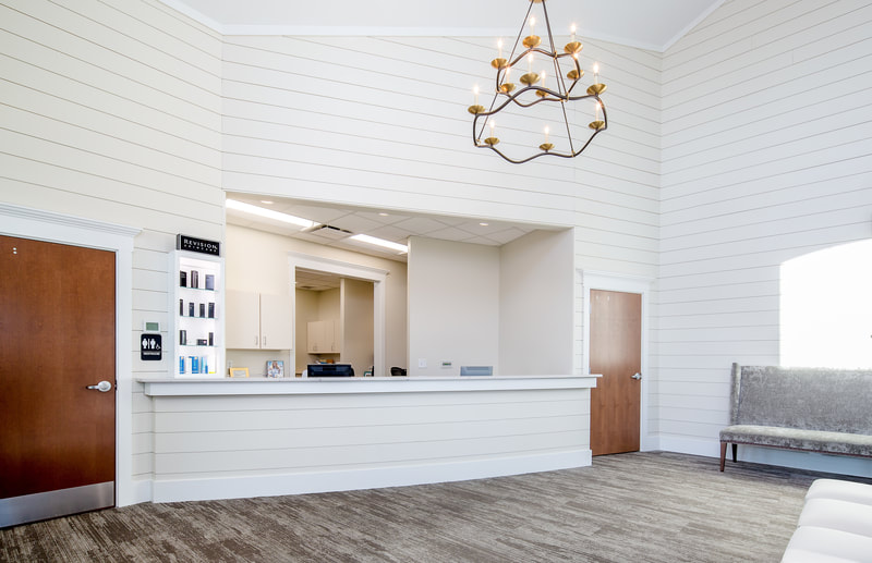 front reception desk of Savannah River Dermatology with rustic chandelier, grey tonal carpeting, and built in lighted shelving for skincare products